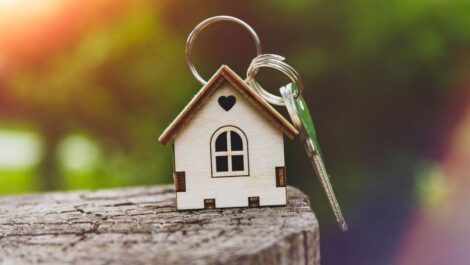Closeup of a wooden house keychain sitting on a log.