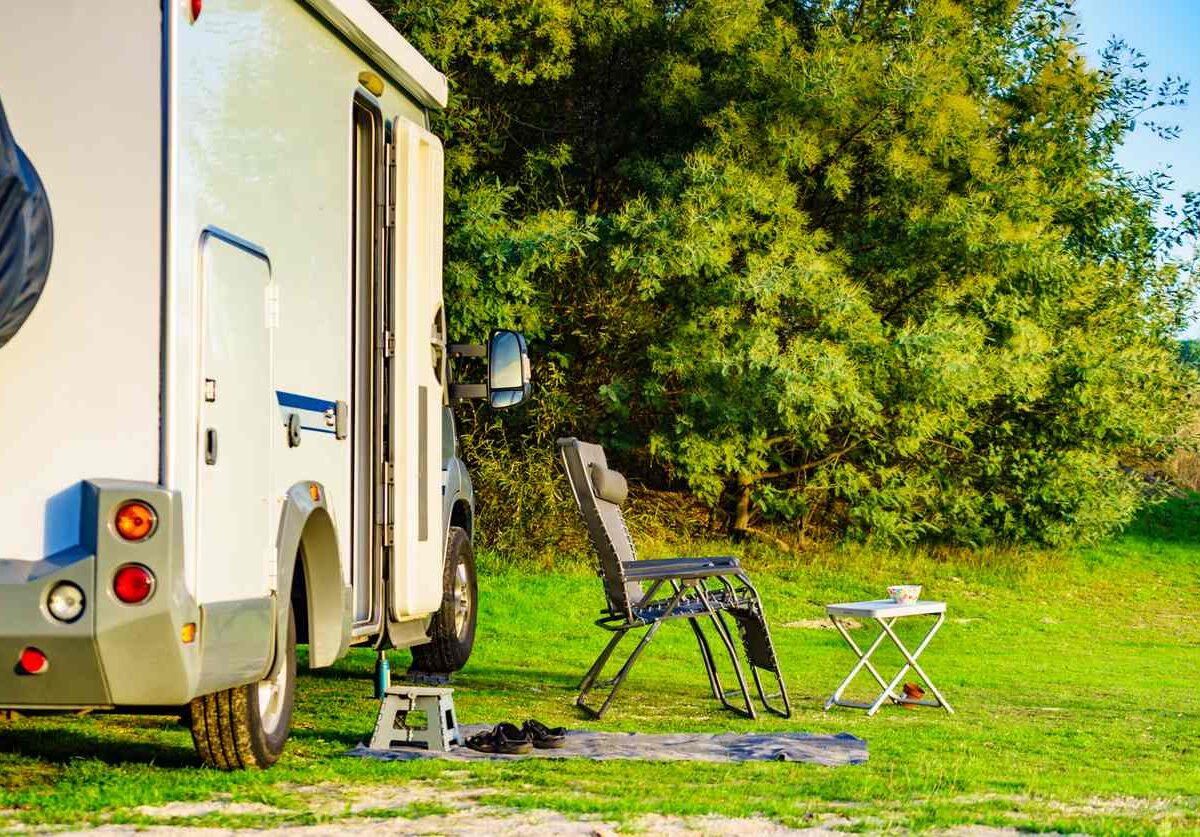 An RV campsite on a green natural area with a lawn chair and table set up.