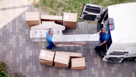 Two movers carry a large piece of furniture into a moving van.